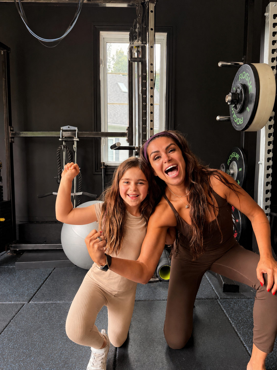 Elle and her daughter smiling together in their home gym